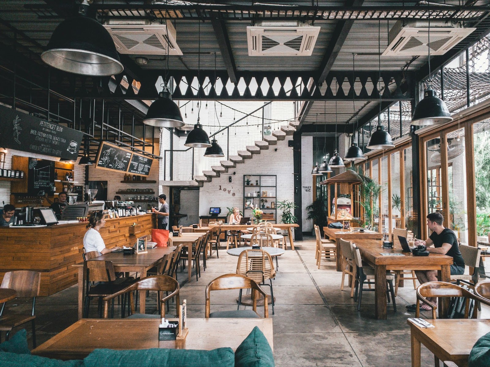 A large rustic cafe with only a few people in it who are working on laptops and drinking coffee.