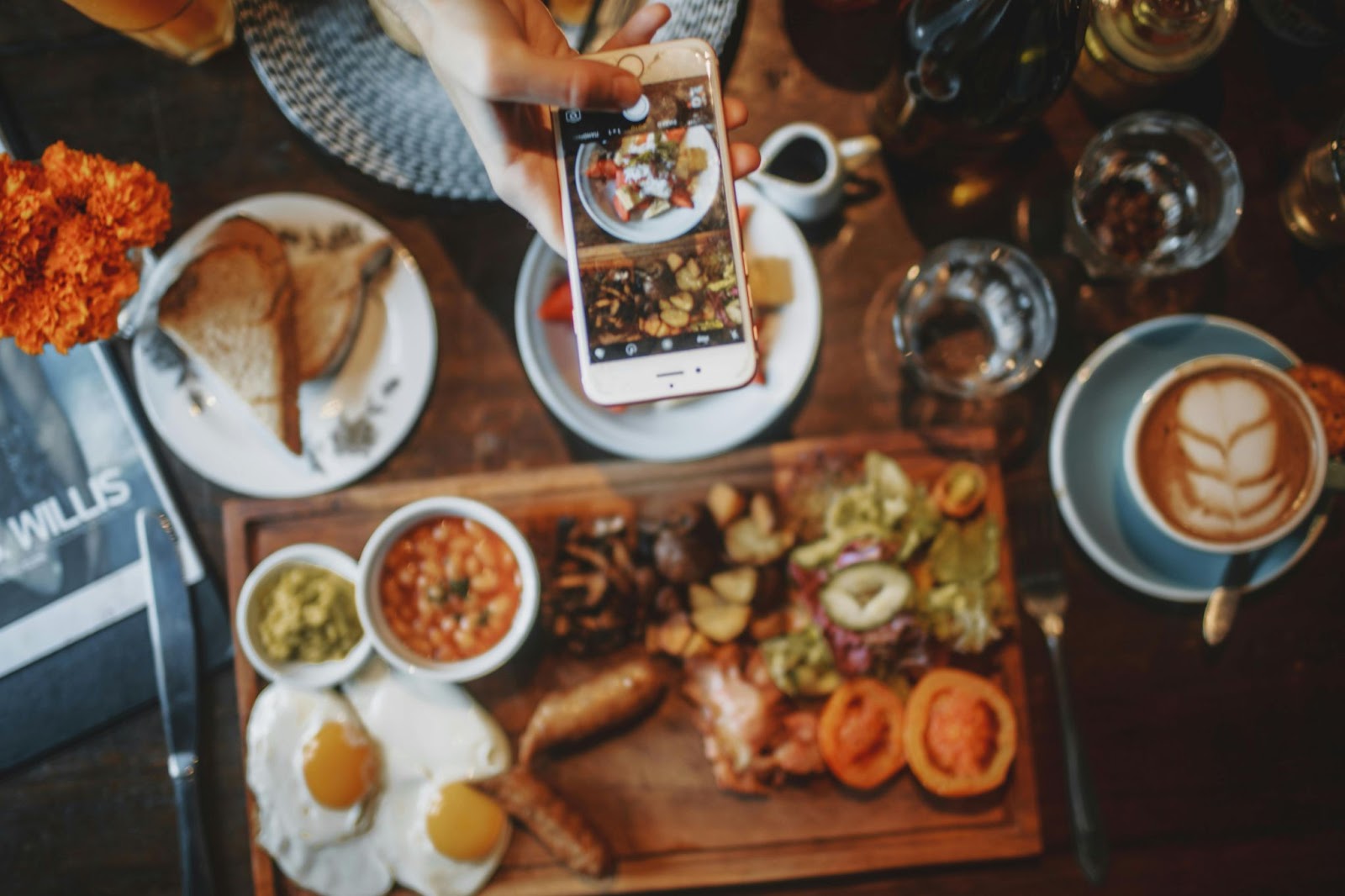 Person using a smart phone to take a photo of breakfast food and coffee in a rustic cafe.