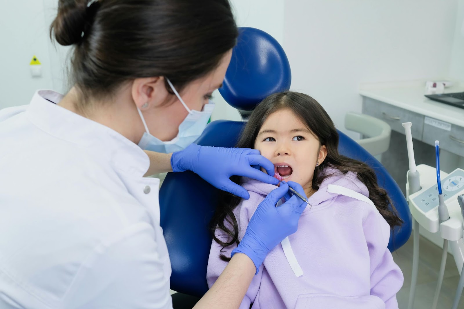 Dental hygienist delicately cleaning child's teeth in a blue chair.