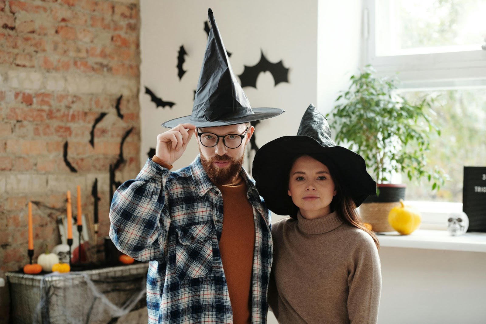 A man and a woman wearing witch hats in a rustic office space that has been decorated with other seasonal elements like candles, pumpkins, and skulls.