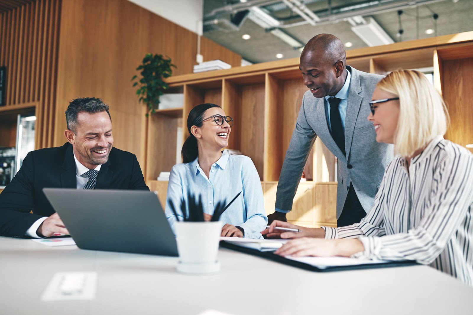 Four professions smiling at a meeting table in a large open office area.