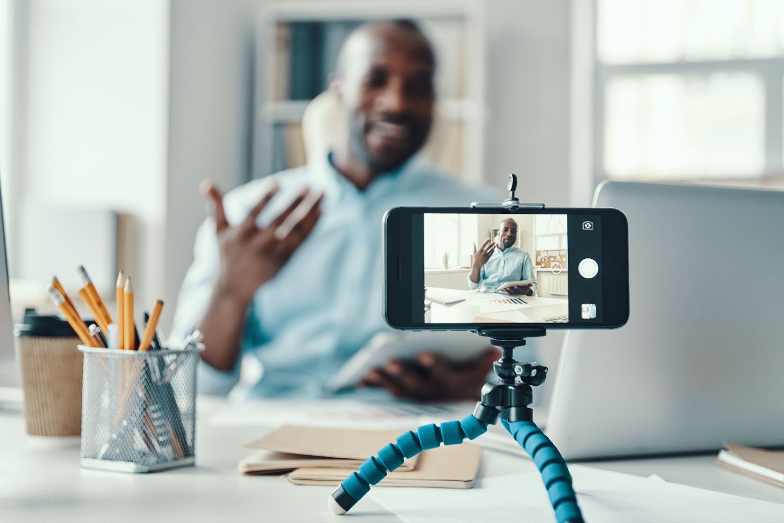 Man recording a video of himself in a brightly lit office on an iphone.