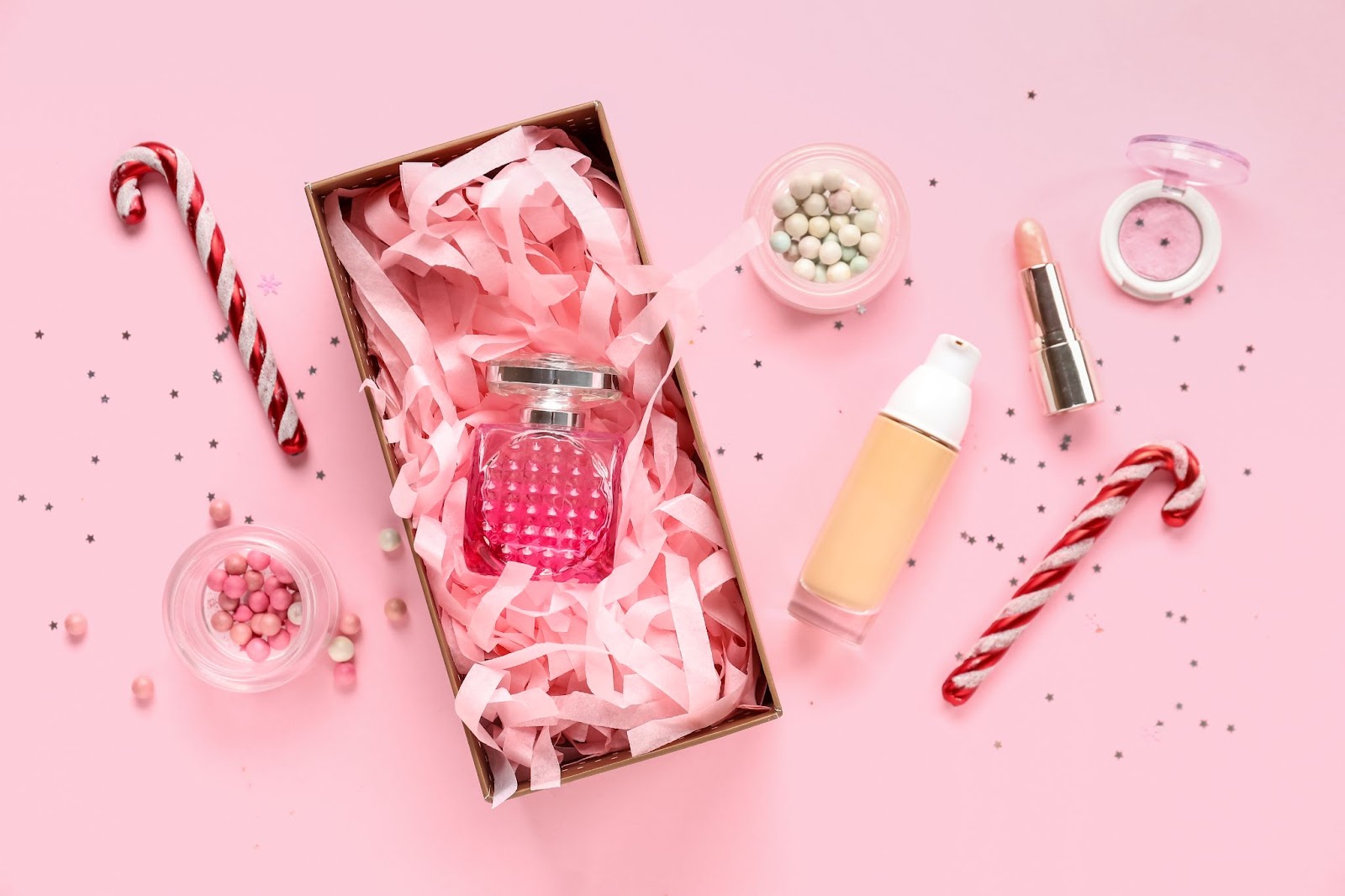 pink background with perfume, candy canes, and misc. Christmas-themed items sitting on top