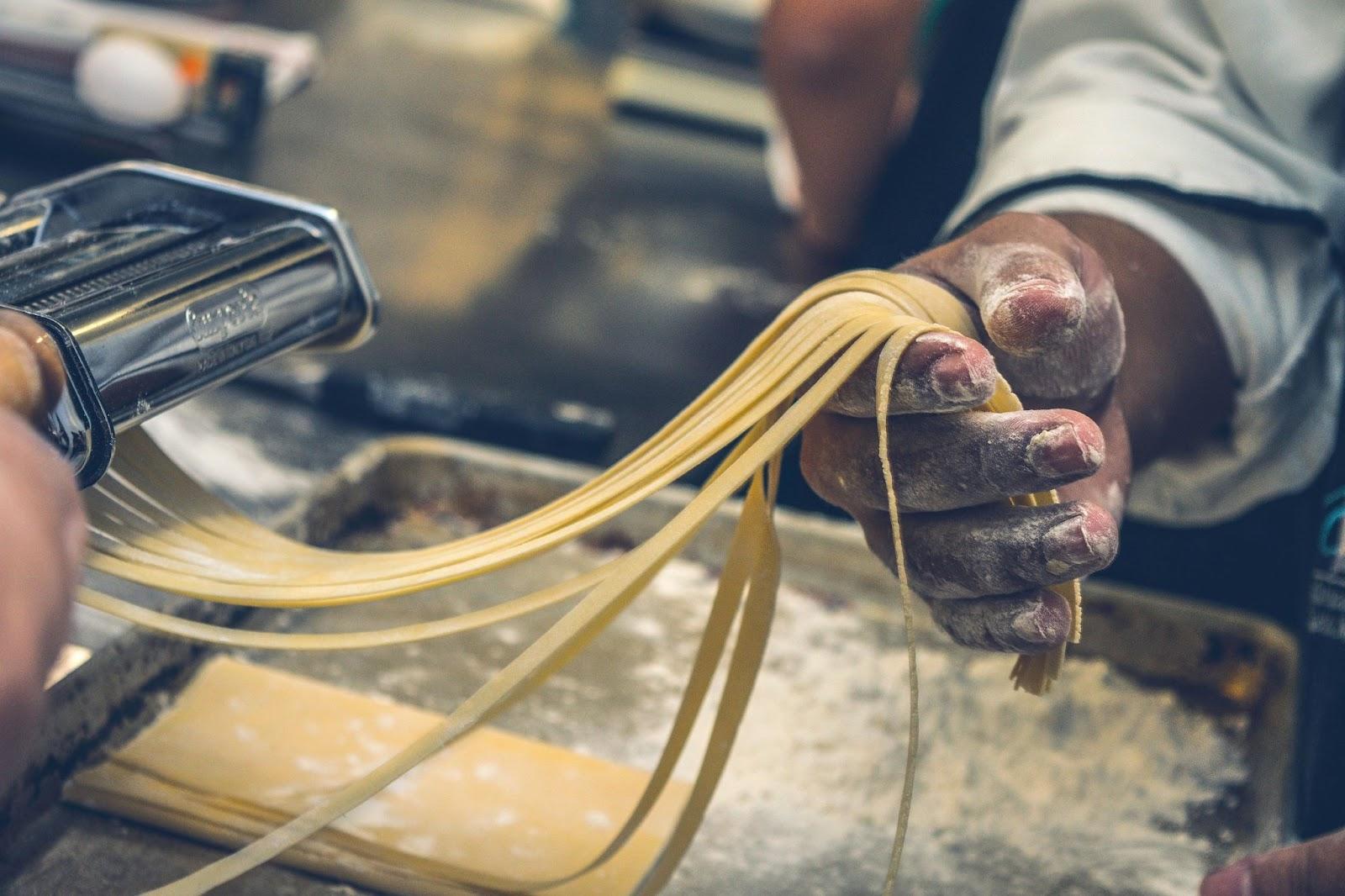 man making pasta in a kitchen, with a closeup of his hands
