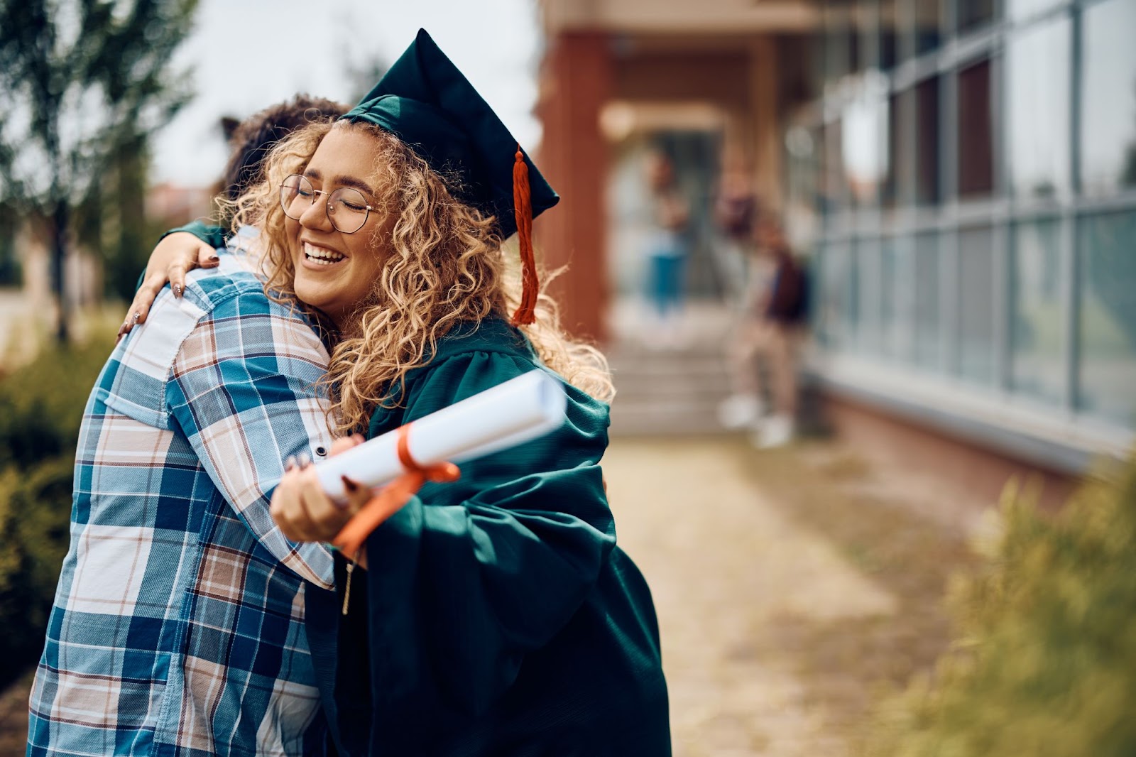 graduate hugging someone and holding a diploma
