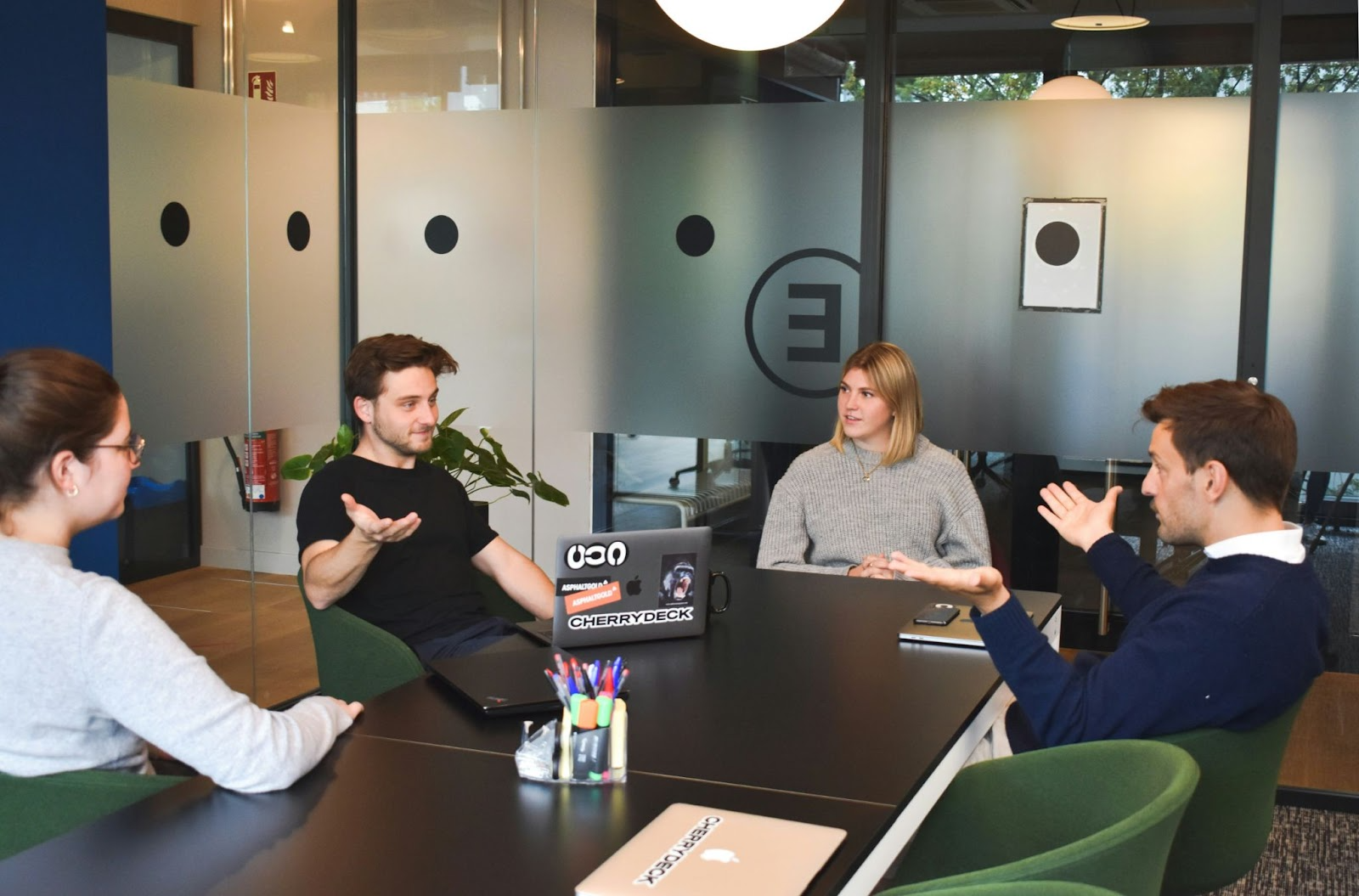 Four people having a meeting in a glass enclosed conference room.